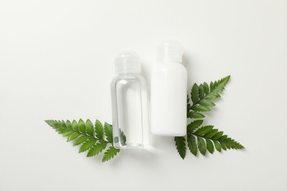 Cosmetic liquids and fern branches on white background, top view