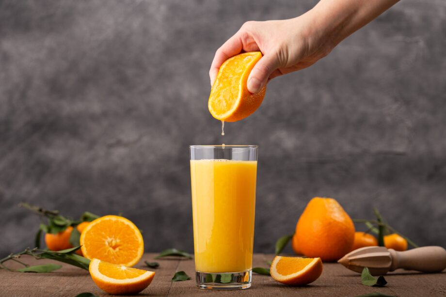 Glass of orange juice and a person squeezing an orange in it