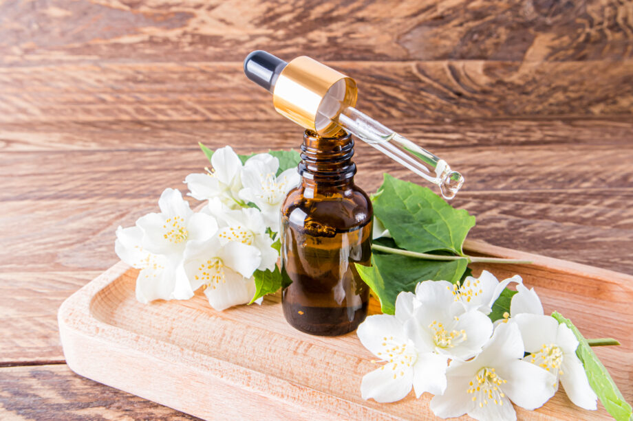 a pipette with natural jasmine oil lies on an open bottle standing on a brown wooden tray among the flowers of jasmine. natural cosmetics.